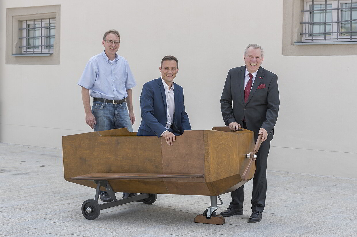 Das Raketenflugzeug zieht am 25. Juli 2018 ins neue Depot des Museums der Bayerischen Geschichte ein: Am Regensburger Donaumarkt freuen sich (v. l. n. r) Peter Zimmermann, Ausbilder Schreiner am HWK-Bildungszentrum Cham, Dr. Andreas Kuhn vom Haus der Bayerischen Geschichte und Jürgen Kilger, Hauptgeschäftsführer HWK Niederbayern-Oberpfalz. Ab Mai 2019 wird das Fluggerät im Museum als Mitmach- und Fotostation eingesetzt. Das Flugzeug ist einem Entwurf von Karl Valentin nachempfunden. Da Karl Valentin selbst Schreiner war, baute er viele seiner Bühnenbilder und –elemente sowie einige (Bühnen-)Flugzeuge in Eigenregie. 